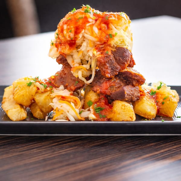 A plate of meat stew with potatoes and coleslaw, topped with red sauce and parsley.