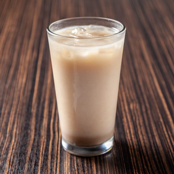 Iced coffee in a clear glass with ice cubes on a dark wooden table.