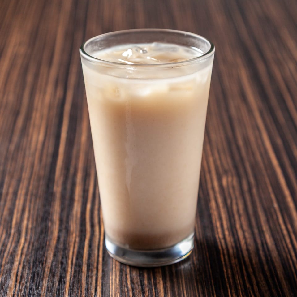 Iced coffee in a clear glass with ice cubes on a dark wooden table.