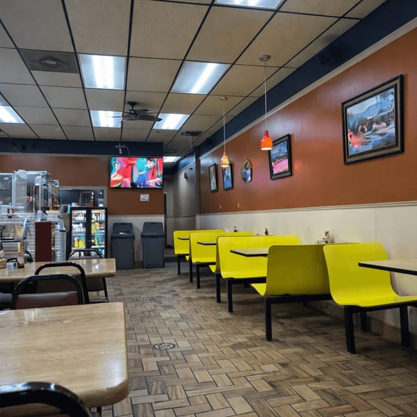 Interior of a casual restaurant with bright yellow booths, wooden tables, and a TV playing in the background.