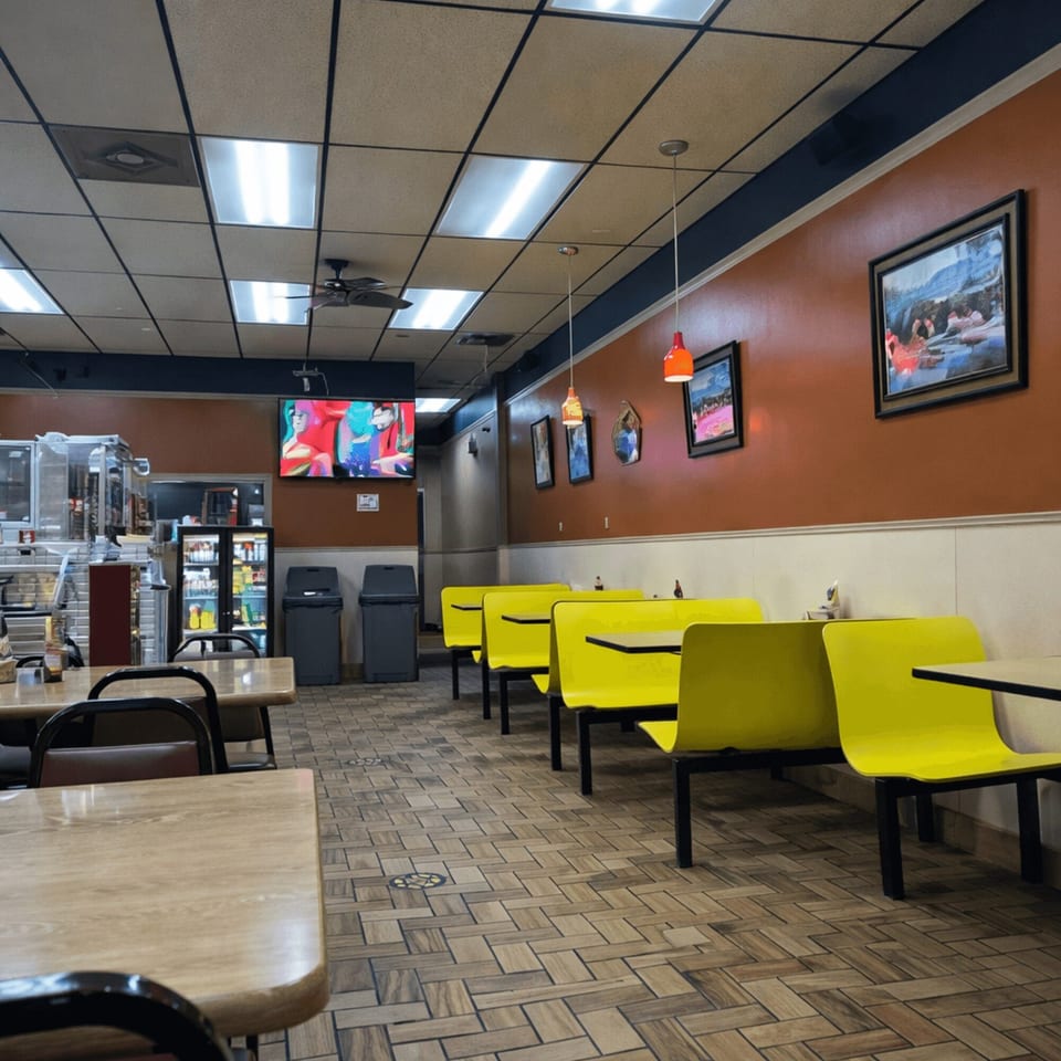 Interior of a casual restaurant with bright yellow booths, wooden tables, and a TV playing in the background.