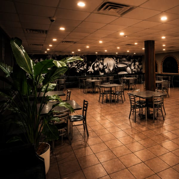 Empty restaurant dining room with tables, chairs, tiled floor, large plant, and a wall mural.