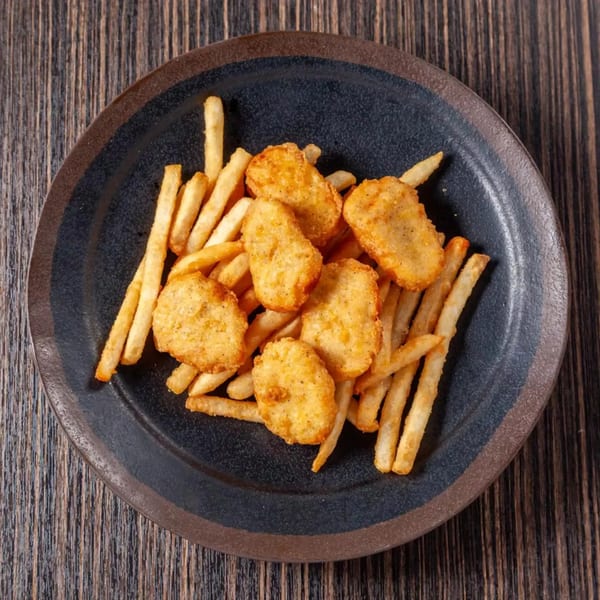 Golden chicken nuggets and crispy french fries served on a dark plate on a wooden table.