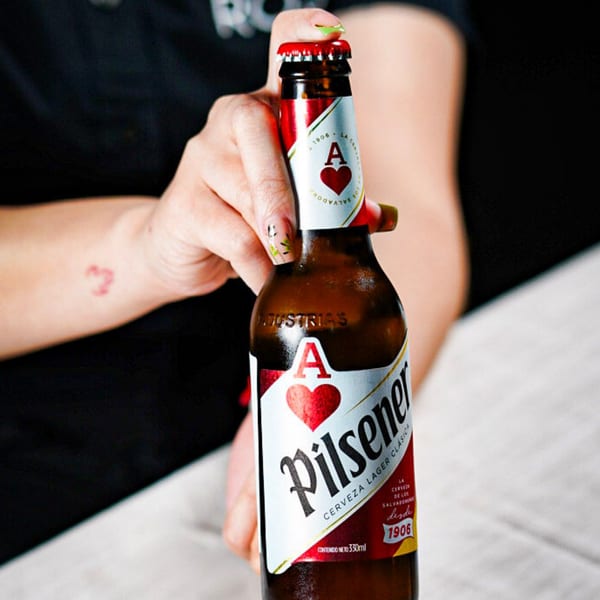 Close-up of a hand holding a Pilsener beer bottle with a red cap and label.
