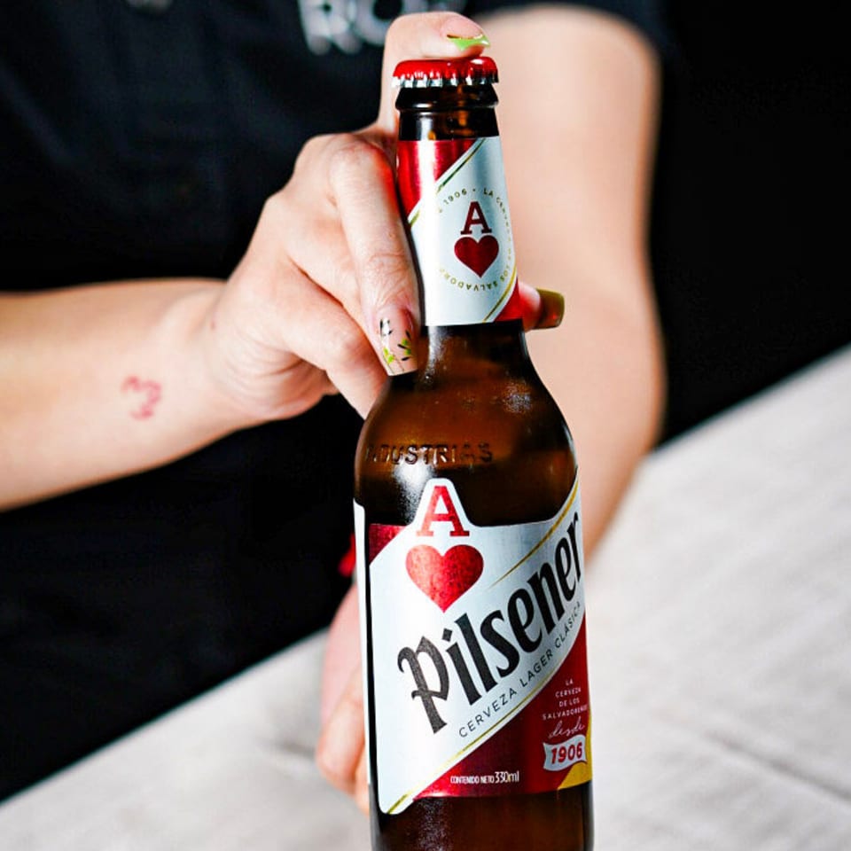 Close-up of a hand holding a Pilsener beer bottle with a red cap and label.