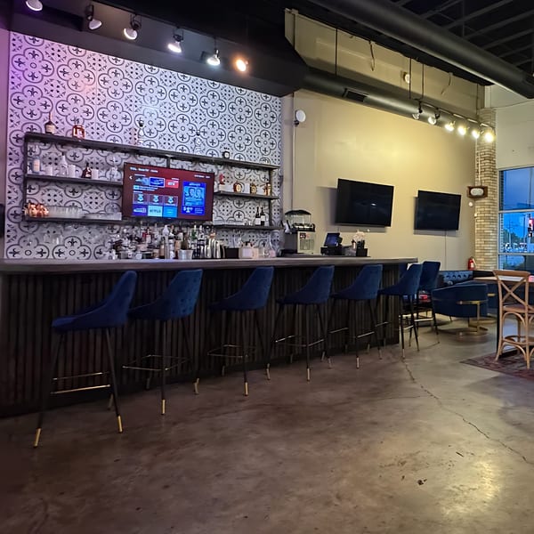 A modern bar area with blue velvet stools, patterned tile, and multiple TVs.