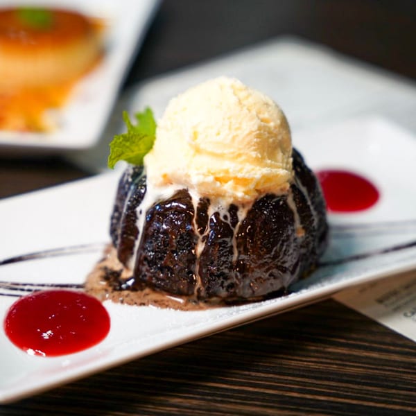 Chocolate lava cake topped with vanilla ice cream, mint, and raspberry sauce on a white plate.