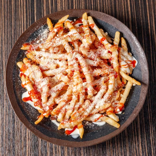 Crispy french fries topped with white sauce, ketchup, and grated cheese on a dark plate.