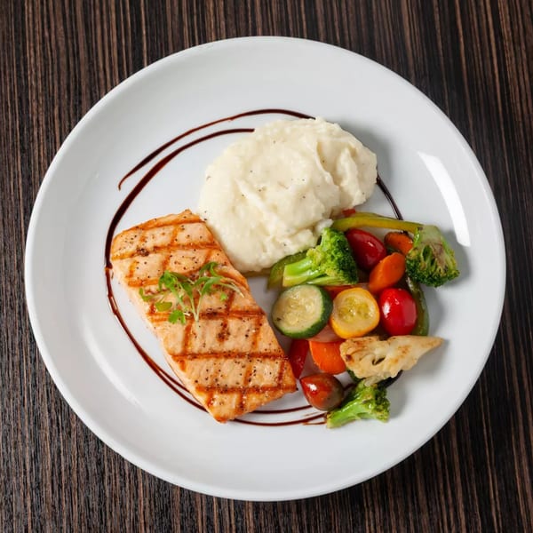Grilled salmon with mashed potatoes and mixed vegetables, drizzled with balsamic glaze on a white plate.