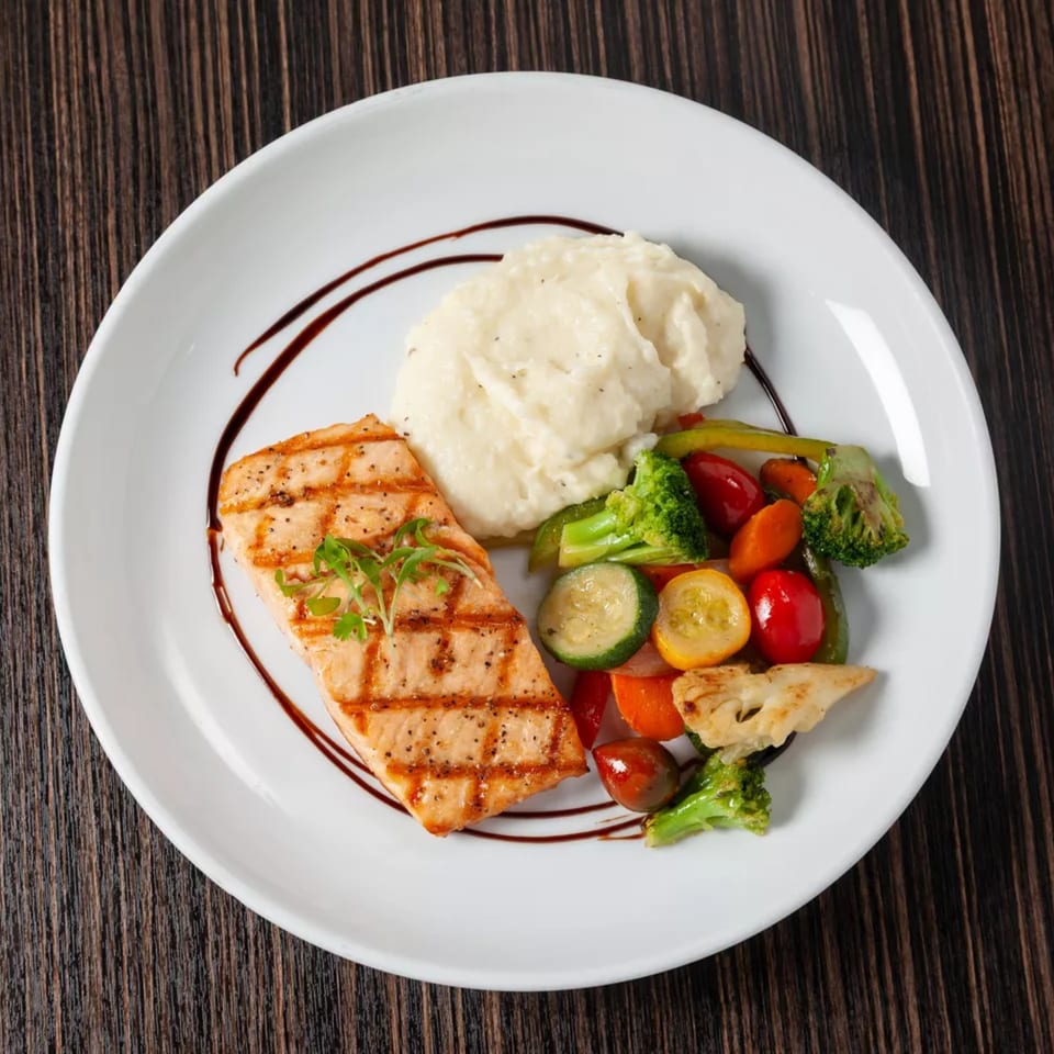 Grilled salmon with mashed potatoes and mixed vegetables, drizzled with balsamic glaze on a white plate.