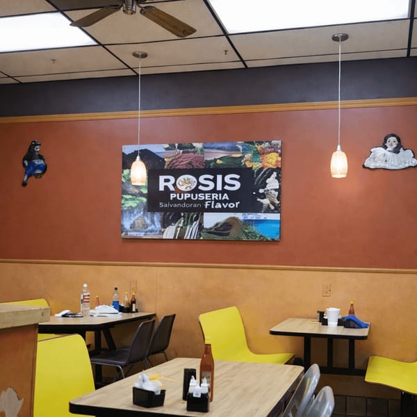 Interior of Rosis Pupuseria with a large sign, tables, yellow chairs, and pendant lights.