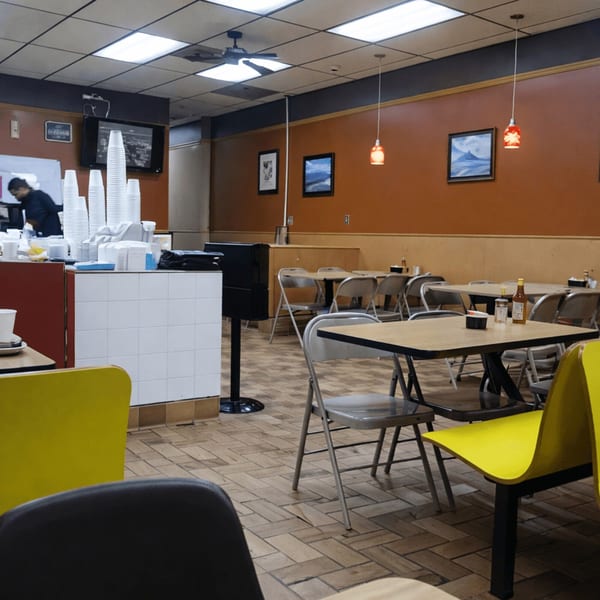 A casual restaurant interior with brown walls, tiled floors, and simple tables with folding chairs.