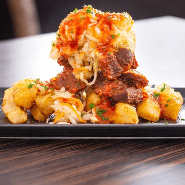 A close-up of a large portion of meat, potatoes, and coleslaw with sauce on a black plate.