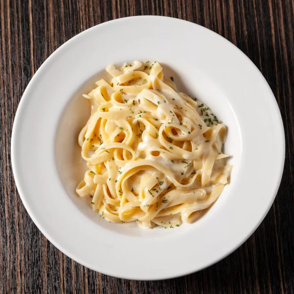 Creamy fettuccine alfredo pasta with parsley flakes in a white bowl on a dark wooden table.