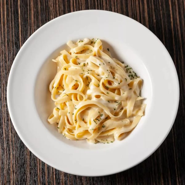 Fettuccine Alfredo pasta with creamy white sauce and green herbs in a white bowl on a wooden table.