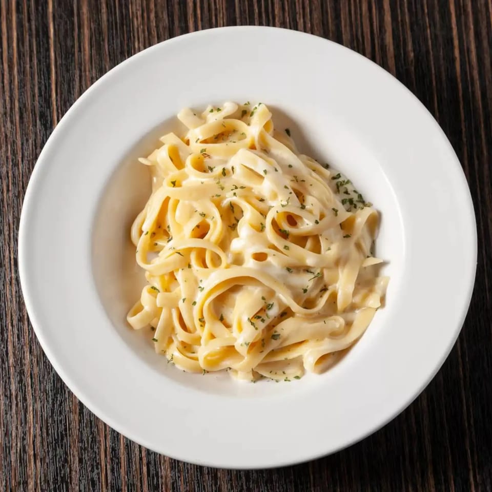 Creamy fettuccine alfredo pasta with parsley in a white bowl on a dark wooden table.