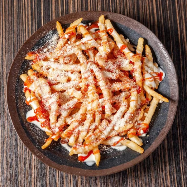A dark plate of french fries topped with white sauce, red sauce, and grated cheese.